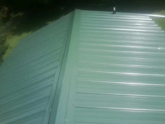 New green metal panels meeting at the ridge of a roof — Flat Roof Repair work by our crew in Lafayette