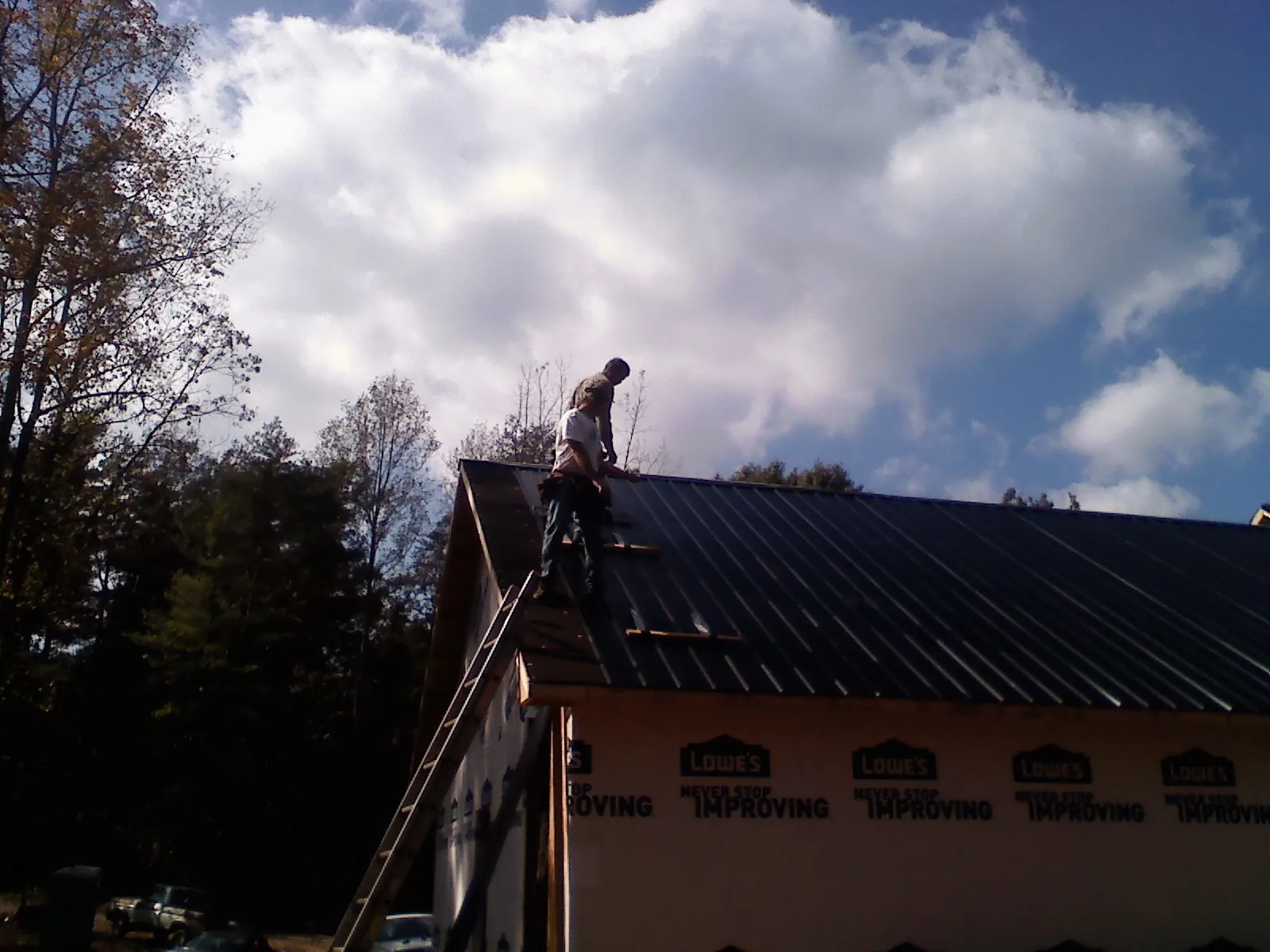 Roofer fastening dark metal panels high against a cloudy sky, from a Roof Inspection job in Lafayette