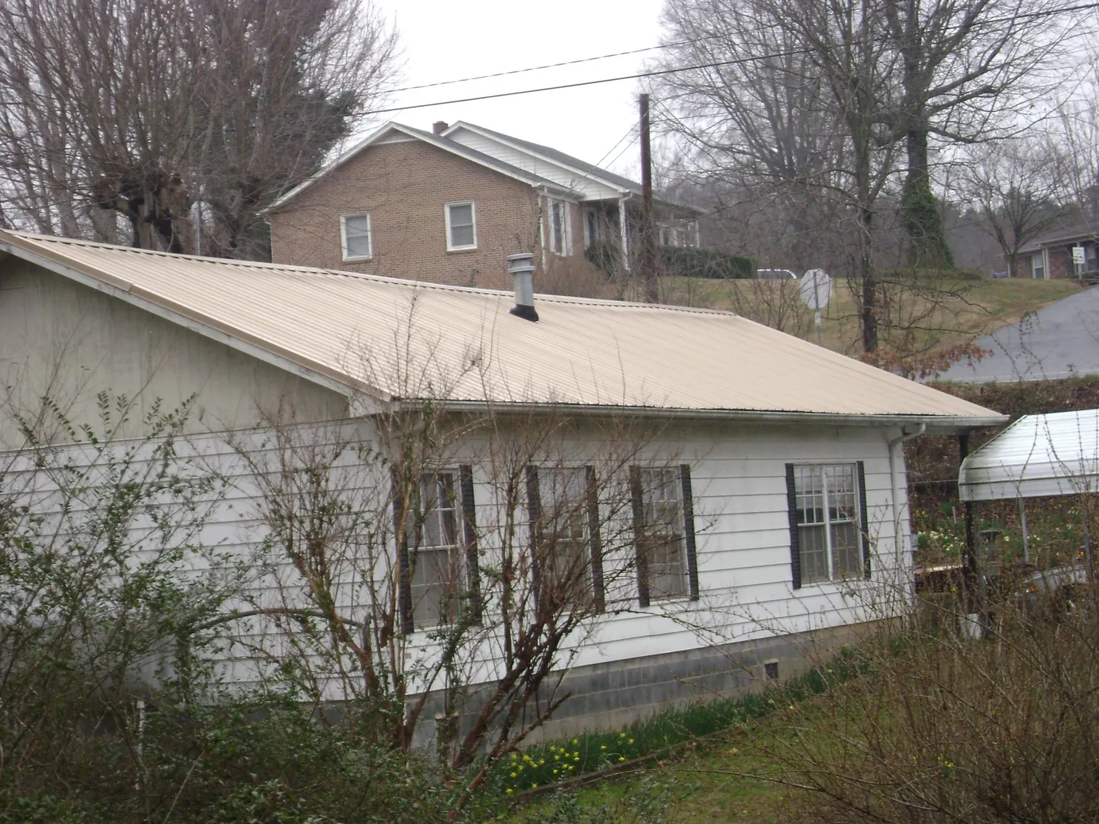 Tan metal roof on a white sided house set into a hillside — Commercial Roofing by Roofing Brothers in Lafayette